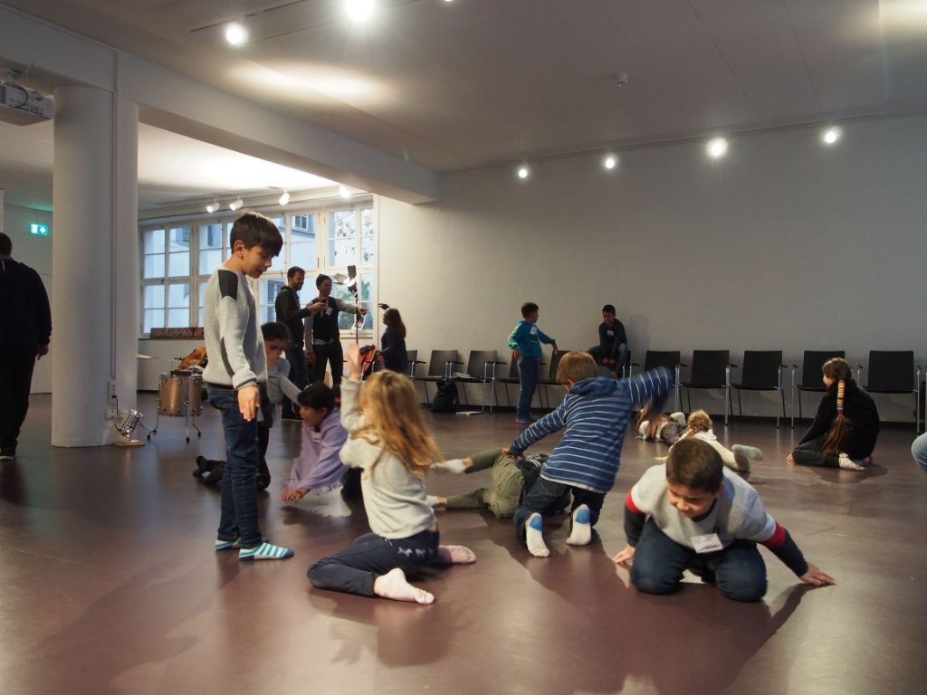 Die Kinder toben sich im Veranstaltungsraum des Museums aus, fünf Kinder kniend, eines stehend. 